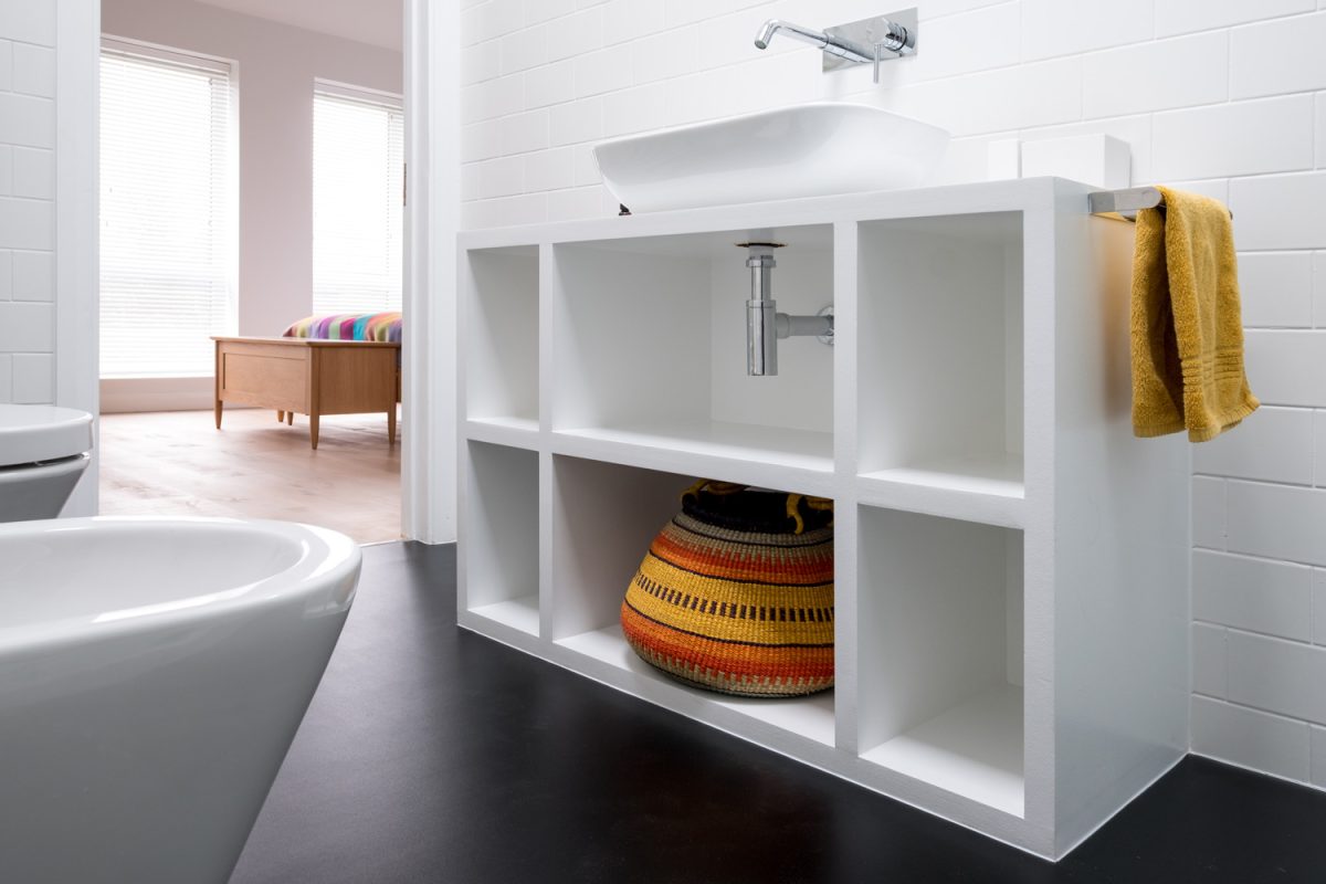 Contemporary white painted MDF bathroom unit, with colourful African bolga basket and black vinyl flooring
