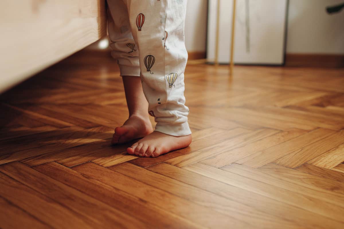 a child's legs in pajamas standing barefoot on the wooden herringbone flooring