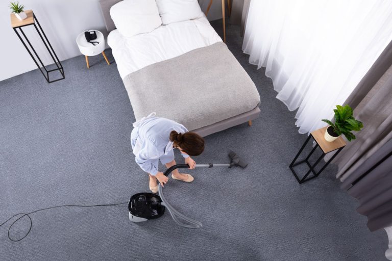 Happy Young Housekeeper Cleaning Carpet With Vacuum Cleaner In Hotel Room, Cleaning Carpet Under The Bed - A Complete 'How To' Guide