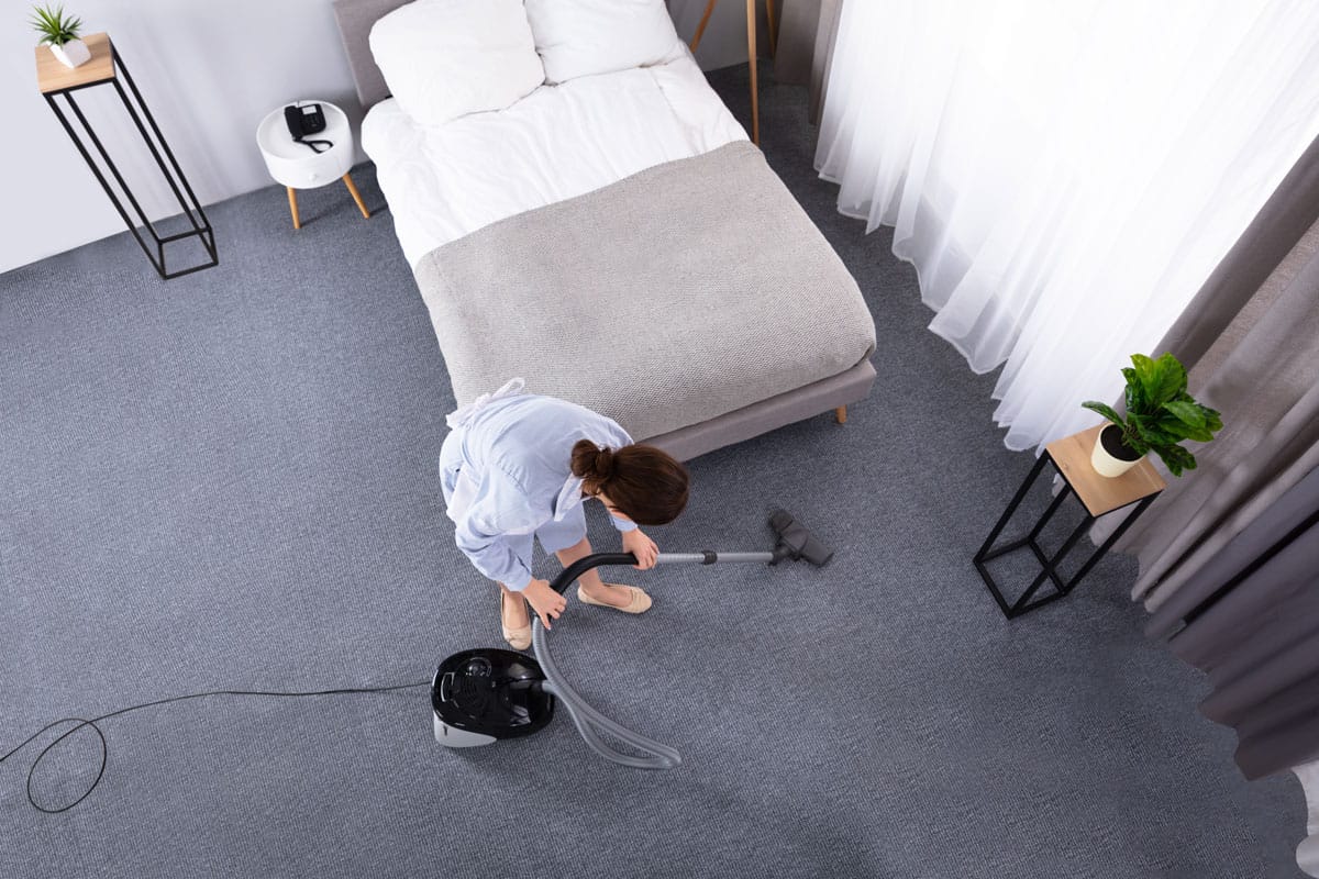 Happy Young Housekeeper Cleaning Carpet With Vacuum Cleaner In Hotel Room