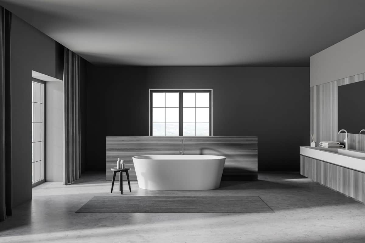 Interior of stylish bathroom with gray and wooden walls, concrete floor, comfortable bathtub and double sink with mirror
