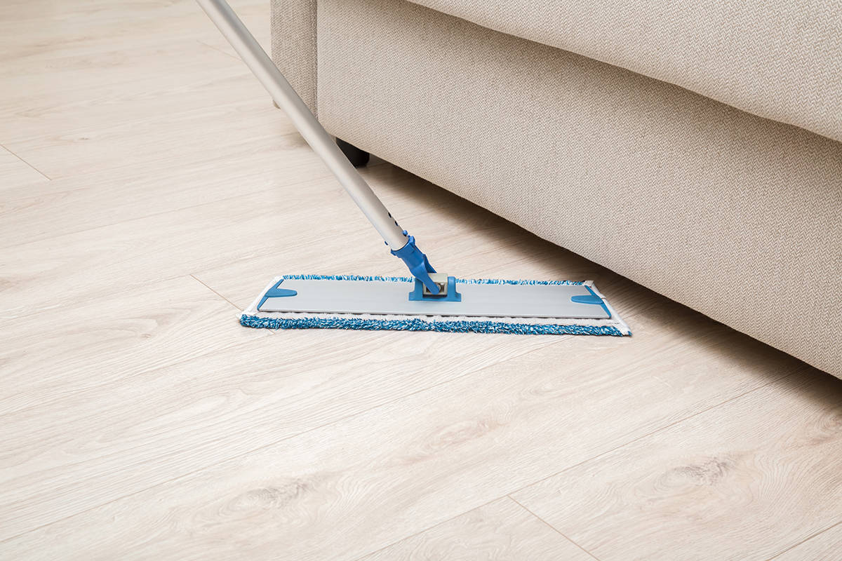 Microfiber mop pad with stick washing light laminate floor under beige sofa at living room