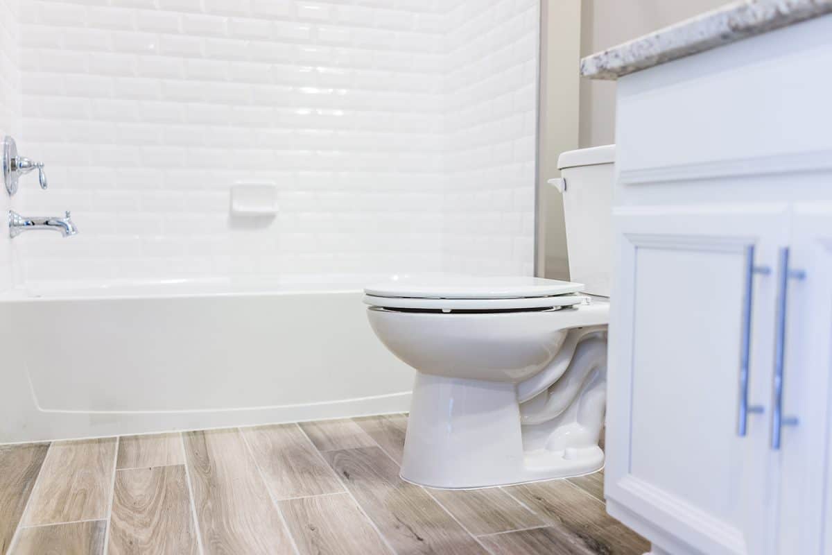 Modern white plain clean toilet bathroom with shower tiles and hardwood floors