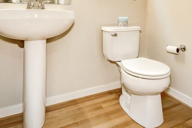 View of washbasin stand and toilet in half bathroom interior, Should Vinyl Flooring Go Under The Toilet?