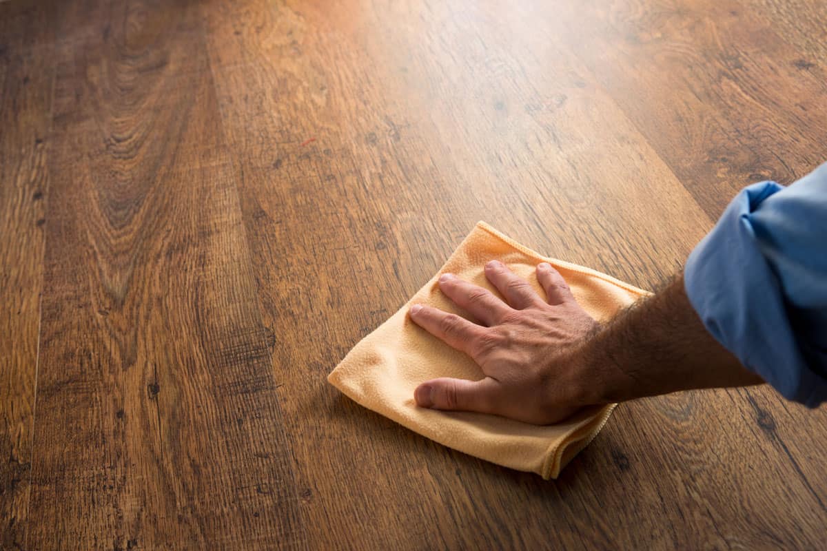 a photo of a man holding a cloth, wiping wax on the wood floor