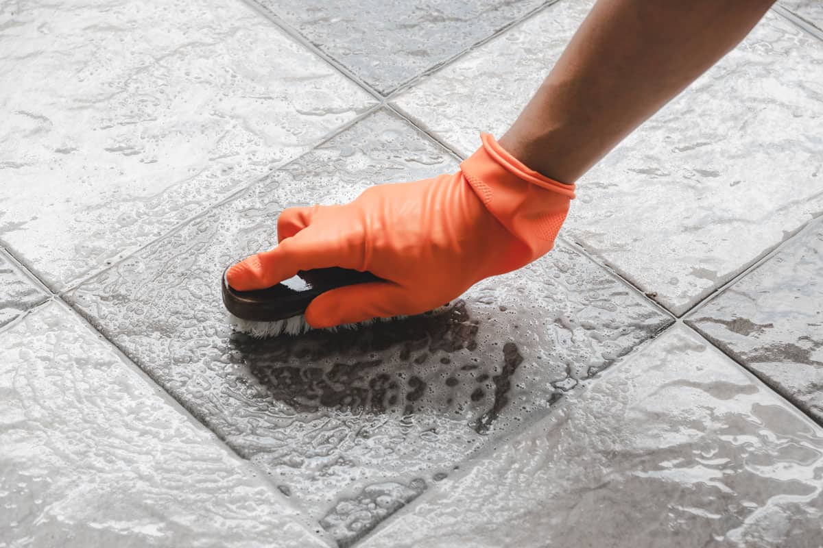 photo of a man wearing safety orange gloves to protect hands from cleaning chemicals on cleaning bathroom floor tile