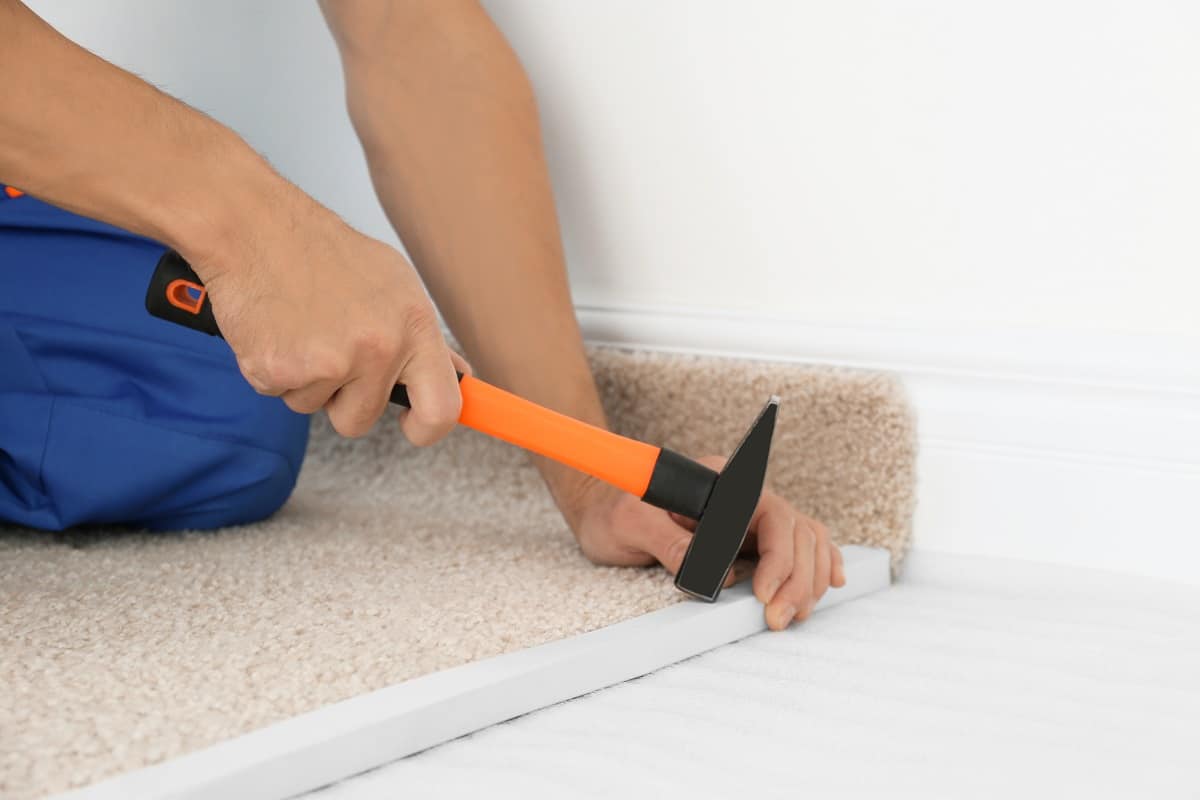 How Do You Attach Carpet To Tack - Worker using hammer while installing new carpet flooring in room
