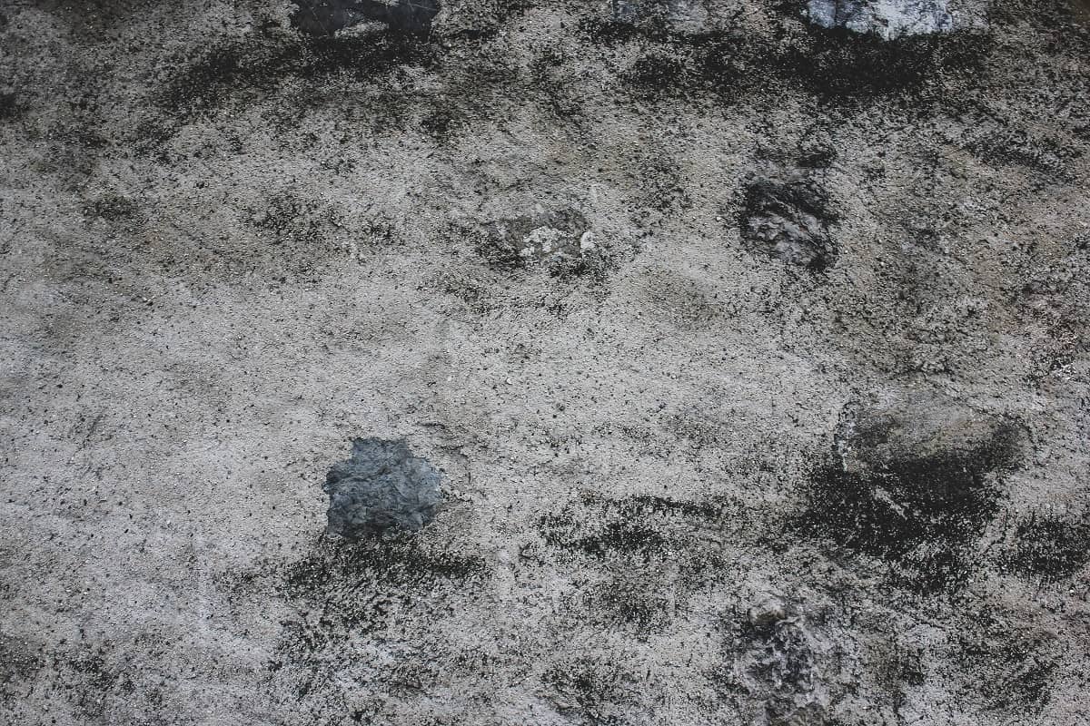 What Is Concrete Floor Delamination - Gray old grungy textured plaster wall with black spots.