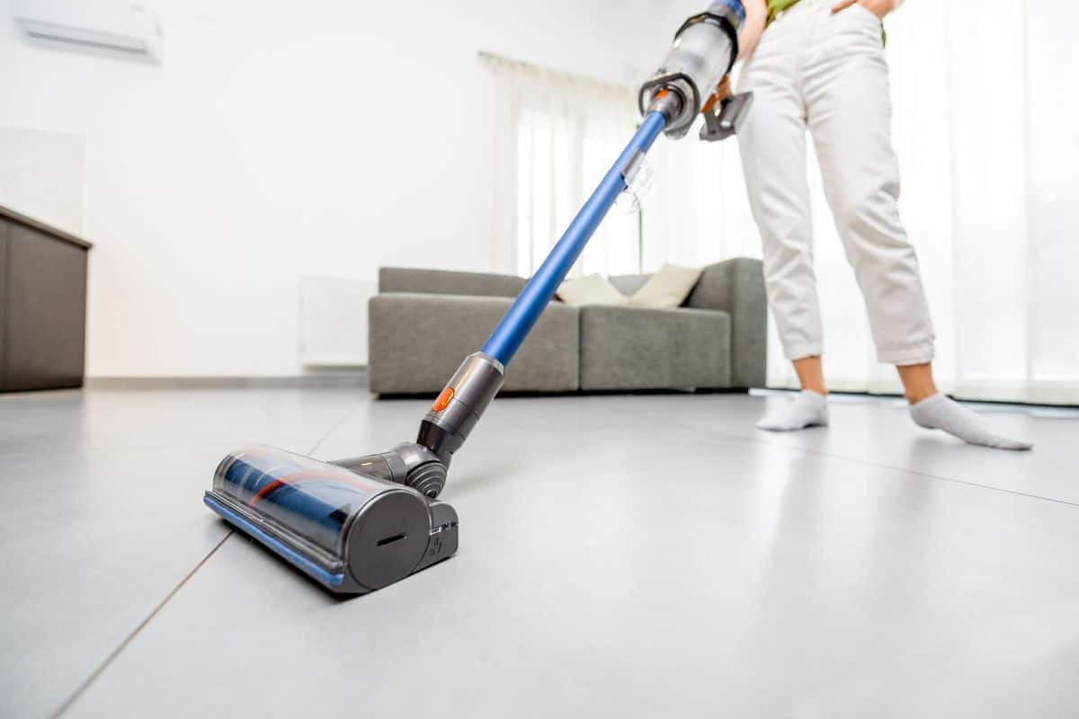 Woman cleaning floor with cordless vacuum cleaner in the modern white living room. Concept of easy cleaning with a wireless vacuum cleaner.