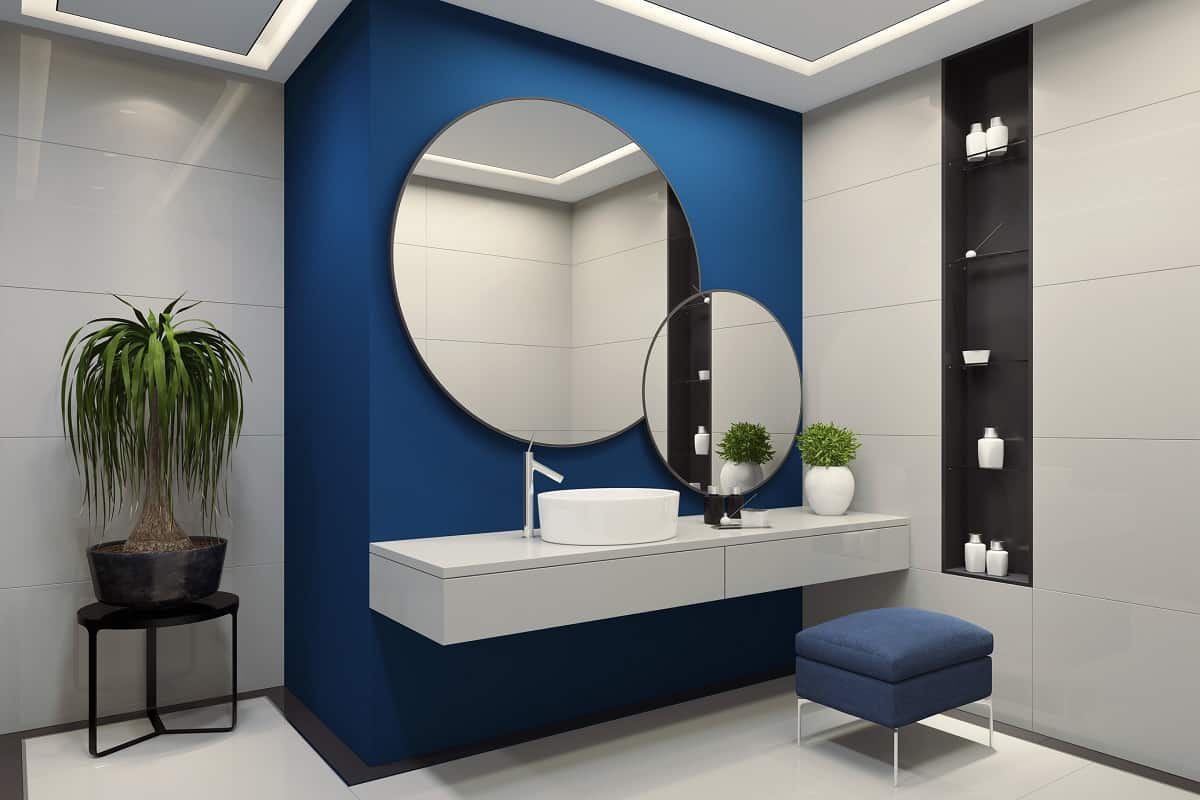 contemporary minimalist blue and white bathroom two round mirrors with black frames are on the royal blue wall.