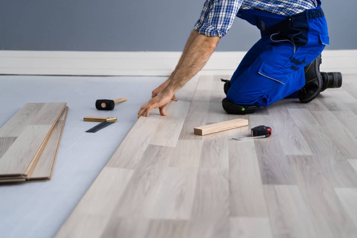 photo of a man installing new wood floor tiles on the room of the house