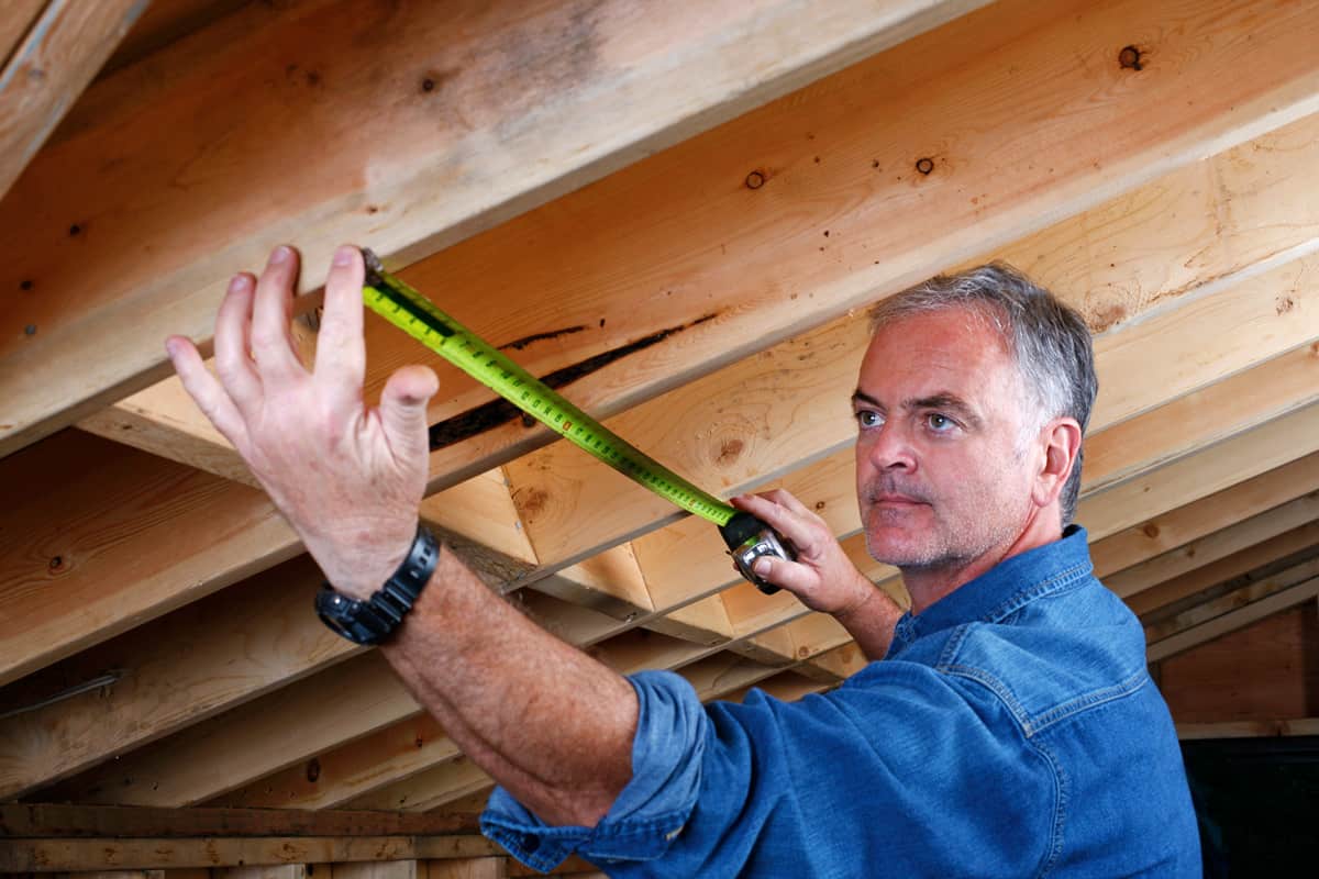 Mature man measuring distance between rafter beams of home addition.