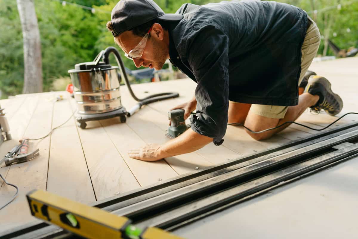 Photo of a carpenter sanding wooden decking in front of the house.