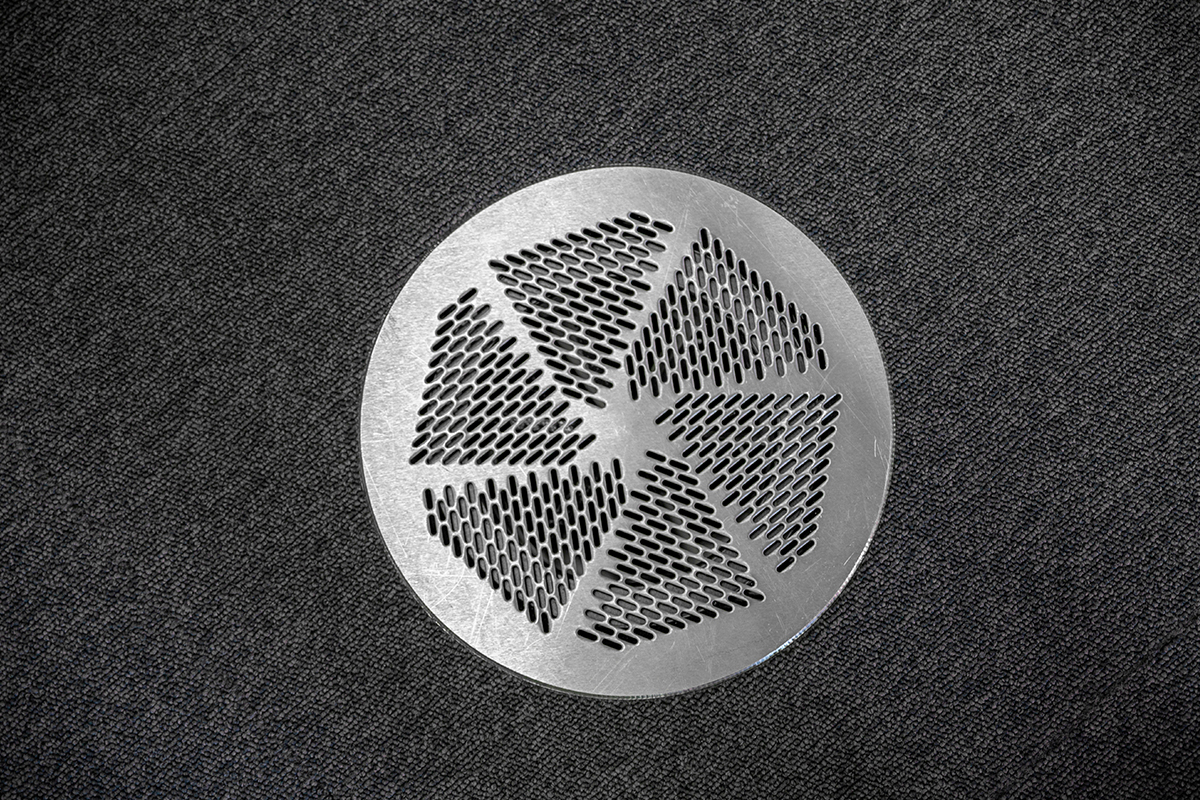 Circular metal air vent in home surrounded by carpet floor